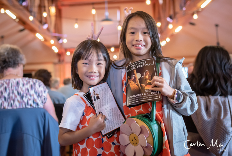 Two young girls holding a program at the Archipelago Collective performance.